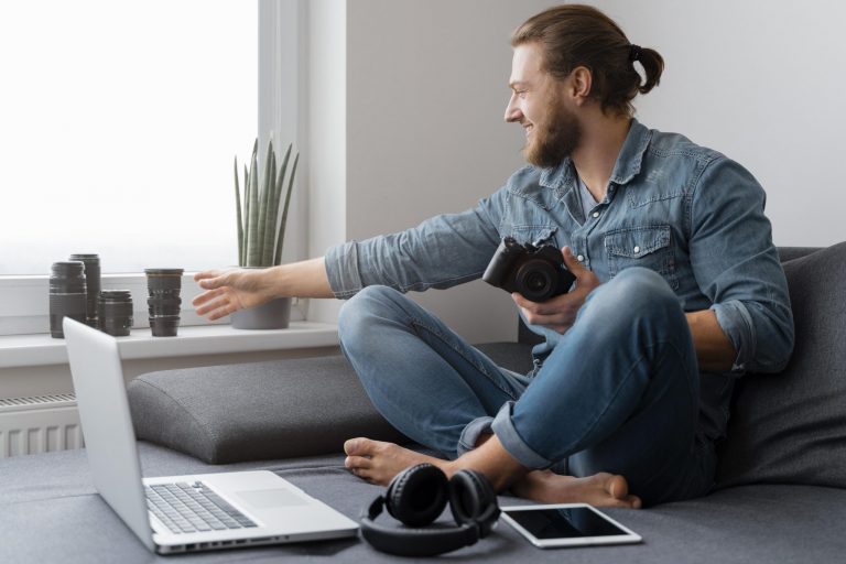 Man in living room wih laptop, camera, headphones, and tablet illustrates blog "Do Pawn Shops Buy Electronics for Cash?"