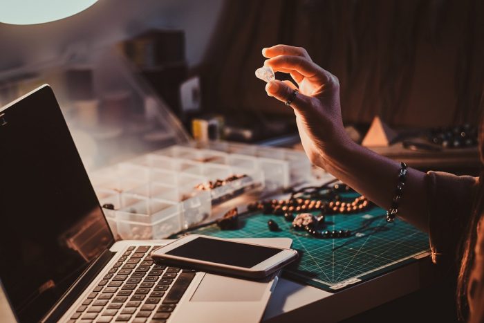 Girl is holding semi precious stone Woman holding stone with phone and laptop by her side illustrates blog "How Do Pawn Shops Determine the Value of an Item?"