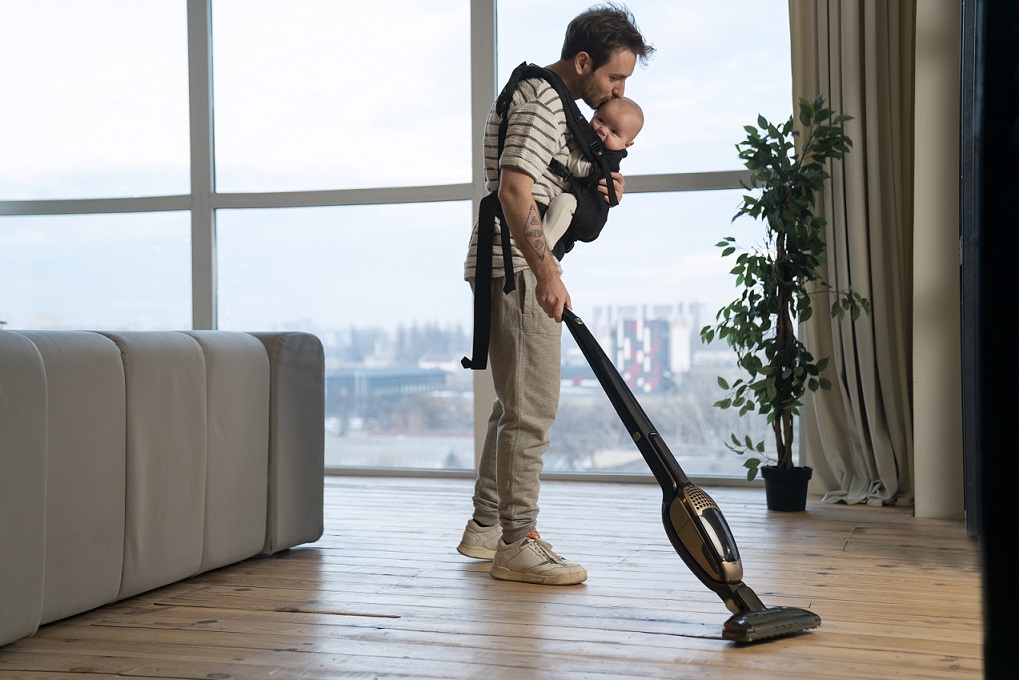Man using vacuum while holding baby illustrates blog "Do pawn shops take vacuums?"